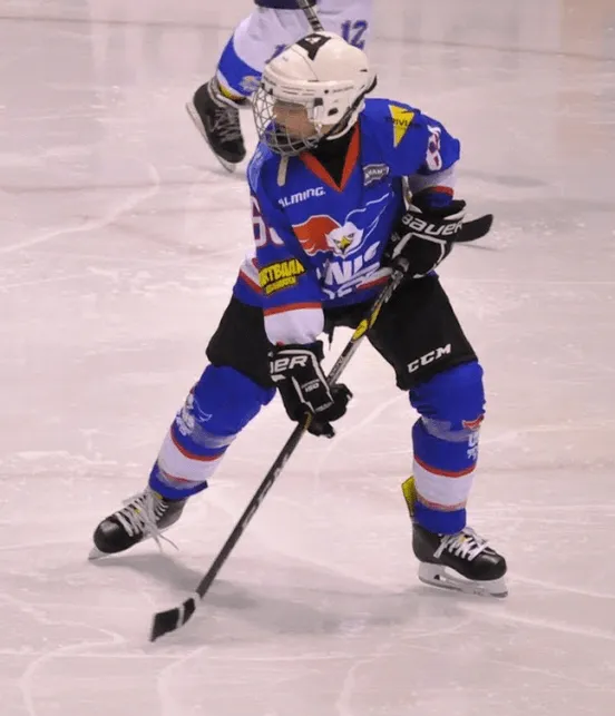 Niek in een blauw ijshockeytenue met helm en stick, in actie op de ijsbaan