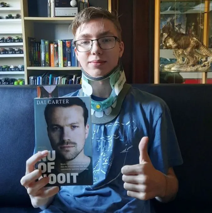 Niek met nekkraag houdt het boek Nu of nooit van Dai Carter vast en steekt zijn duim op
