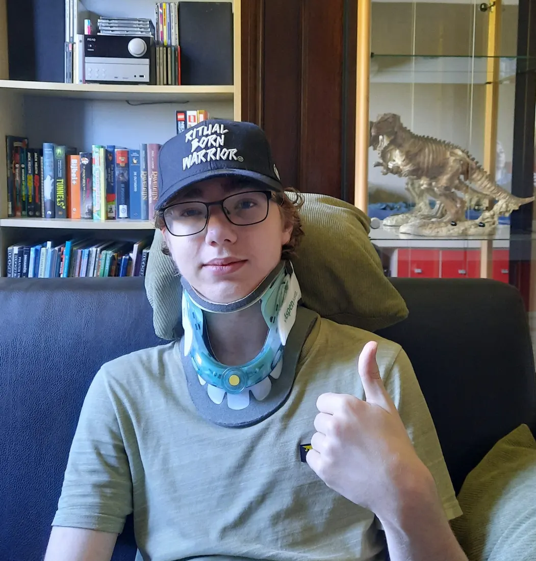 Niek met pet en nekkraag in een stoel, duim omhoog