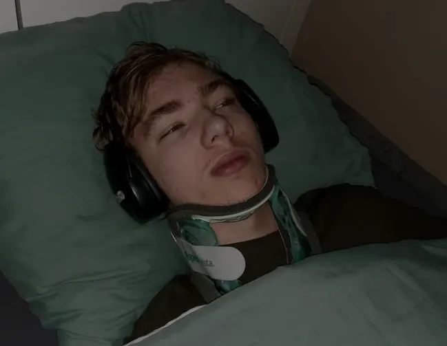 Niek ligt in het donker in bed met een koptelefoon op en zijn nekkraag om