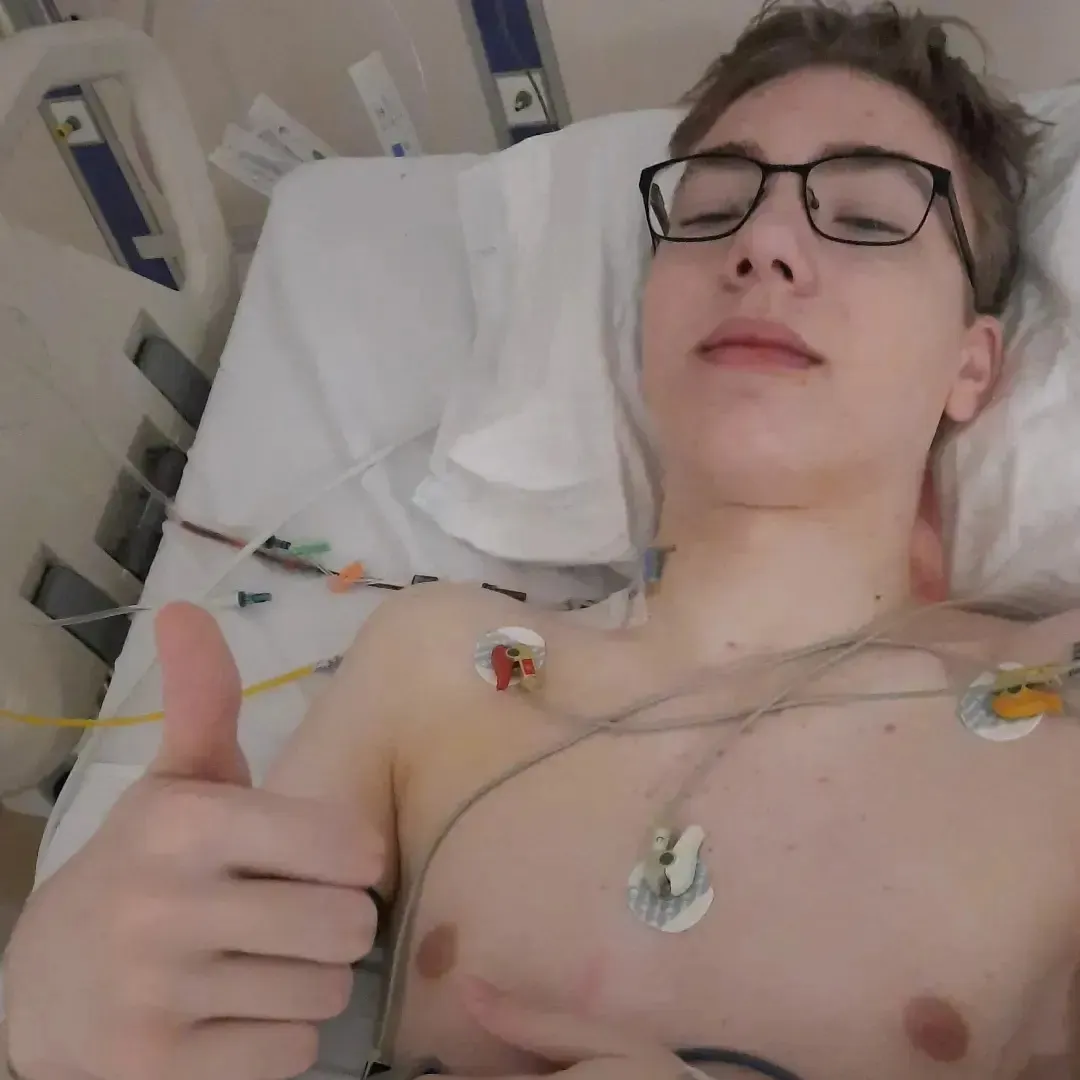 Niek in het ziekenhuisbed na de operatie, met plakkers van de hartbewaking op zijn borst en zijn duim omhoog