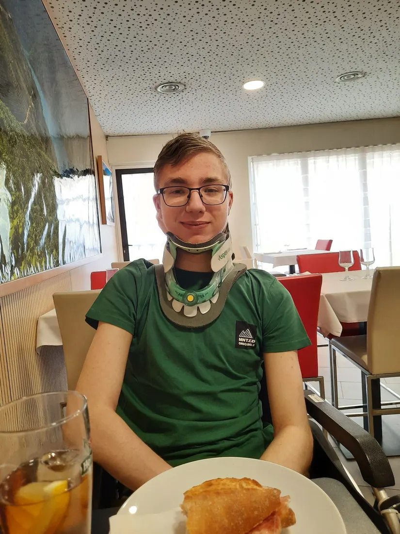 Niek met nekkraag aan een restauranttafel met een broodje voor zich