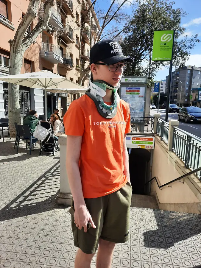 Niek staat met nekkraag en pet in de zon op een stoep in Barcelona