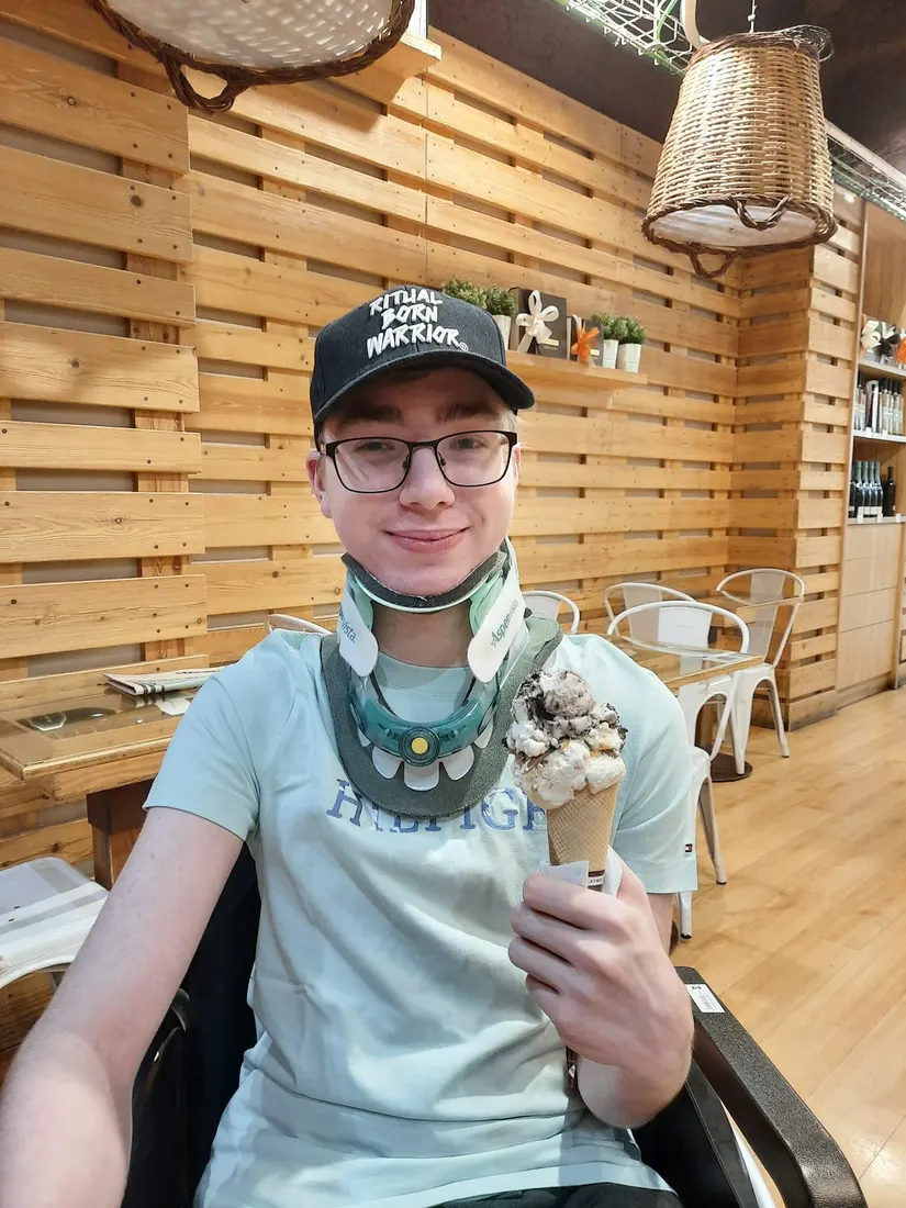 Niek met nekkraag en pet, met een ijsje in zijn hand in een ijssalon in Barcelona