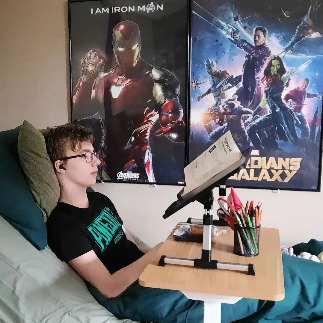 Niek thuis in bed met een verstelbaar tafeltje voor zich, onder filmposters van Iron Man en Guardians of the Galaxy
