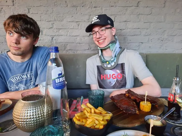 Niek met nekkraag aan tafel in een restaurant, met spareribs en friet voor zich